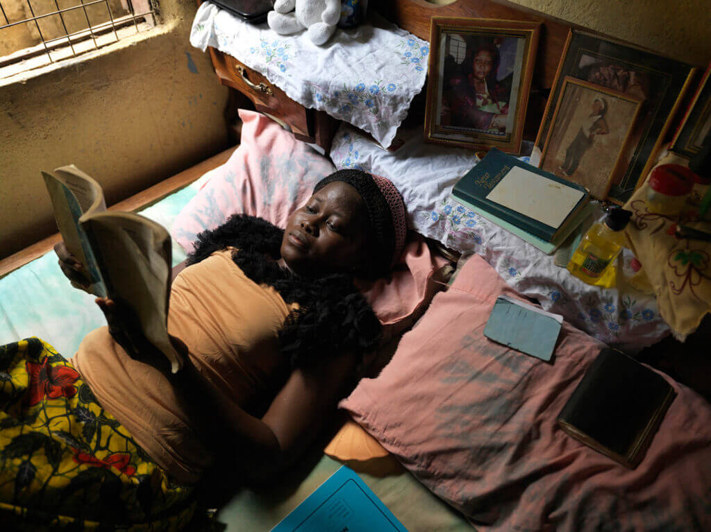 A young woman lays in bed reading a book. 