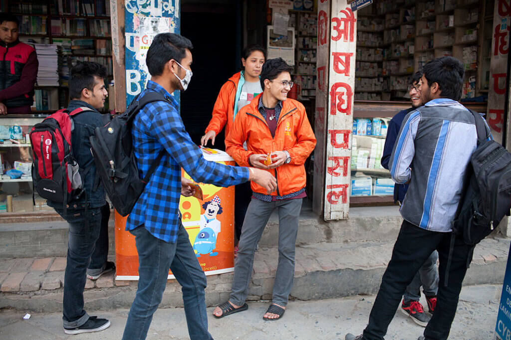 Two volunteers in orange jackets on a busy street, talking to passers-by about sexual health.