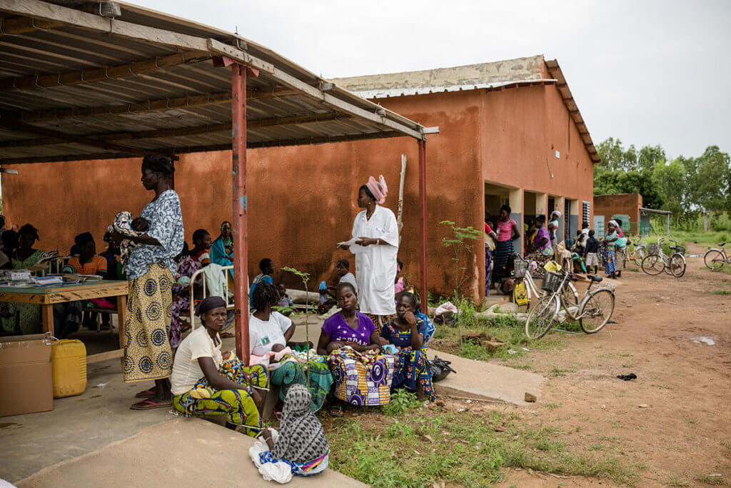 A group of women sit outside under a metal pavilion.