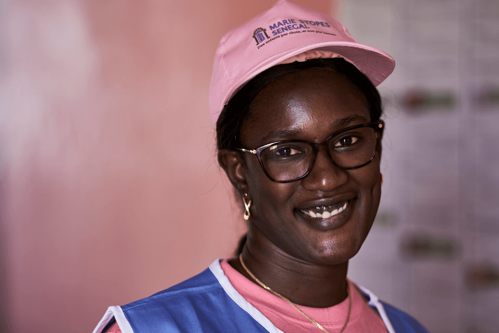 Dias, a Senegalese woman wearing a pink hat and glasses, smiles at the camera.