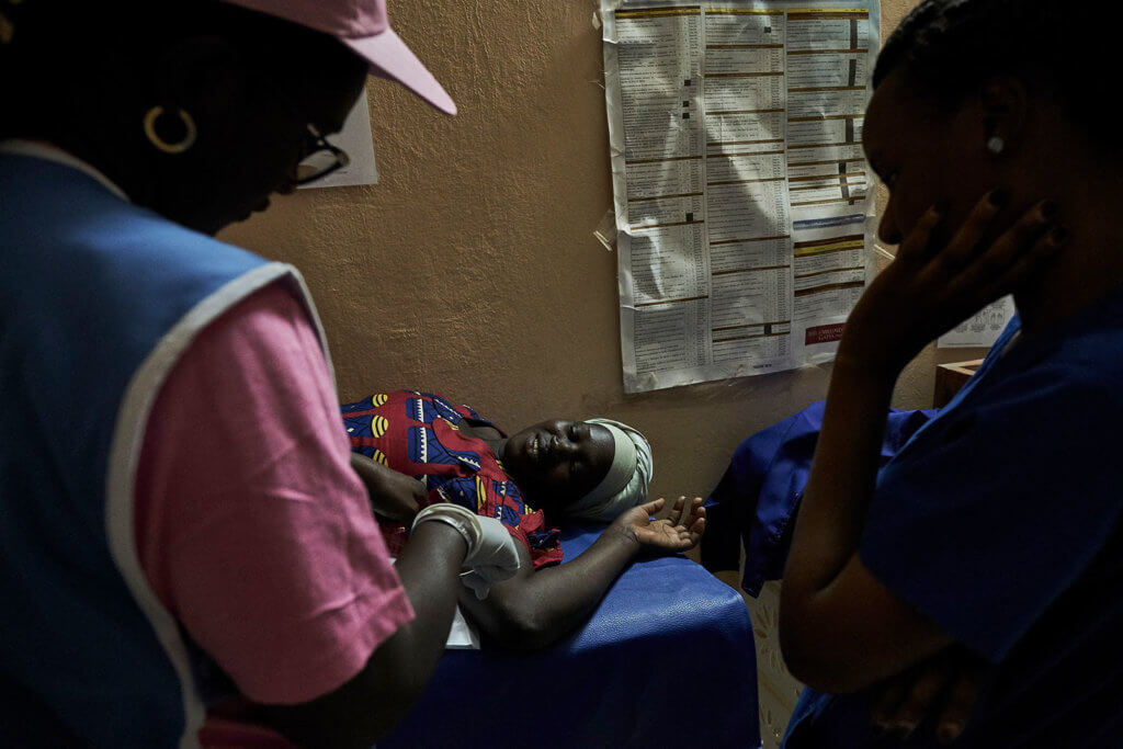 Dias, a nurse in a pink shirt and hat, inserts a contraceptive implant in the arm of a smiling woman.