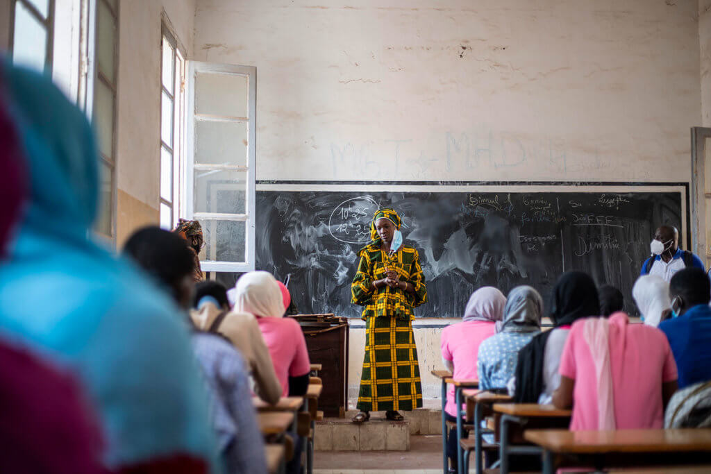 A teacher stands in front of a classroom full of students in Senegal. She supports girls' education by teaching her students about reproductive health.