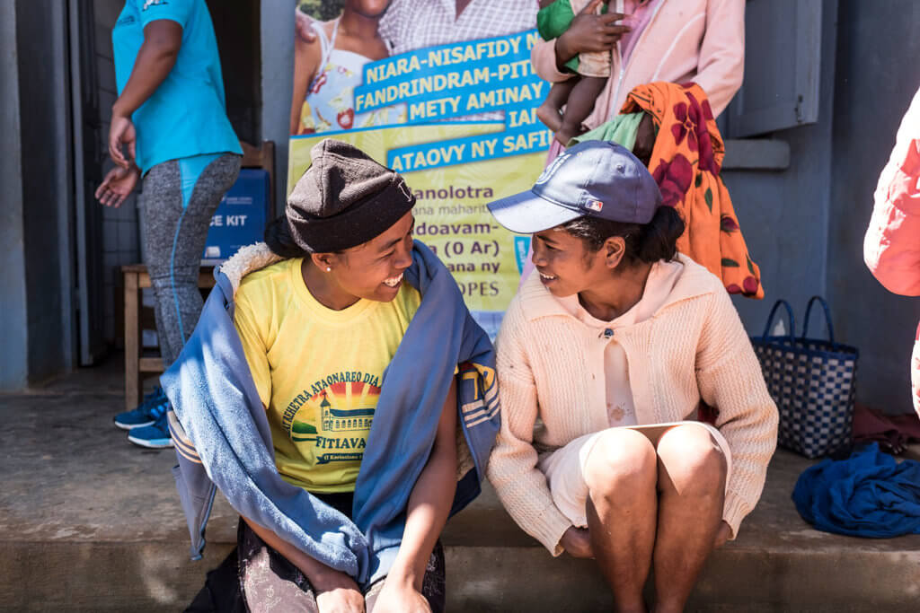 Two women from Madagascar sit on a step and smile at each other. Child marriage remains widespread in Madagascar.