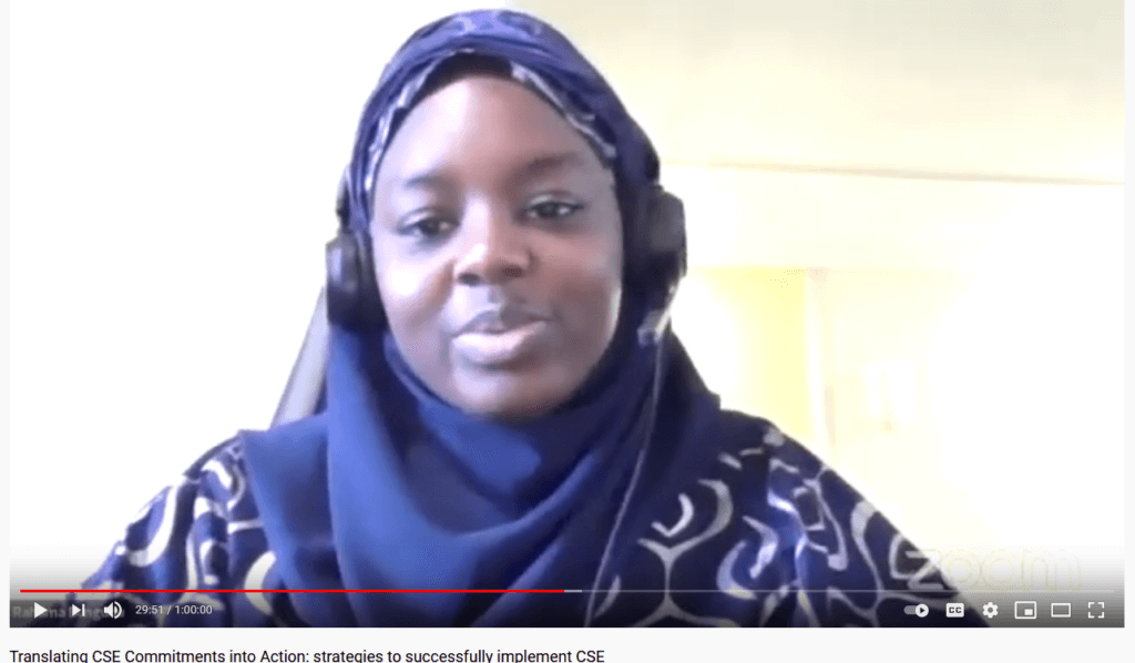 A Nigerian woman in a headscarf and headphones speaks on video about keeping girls in school.