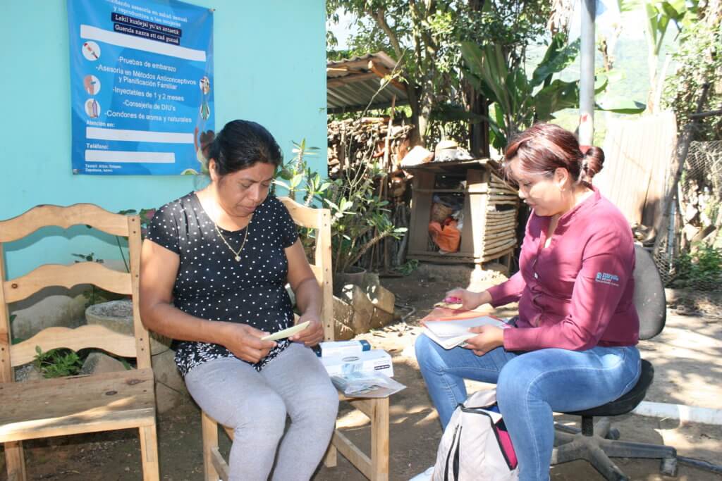 MSI team member Yadira sits with a traditional midwife, passing her boxes of contraceptives.