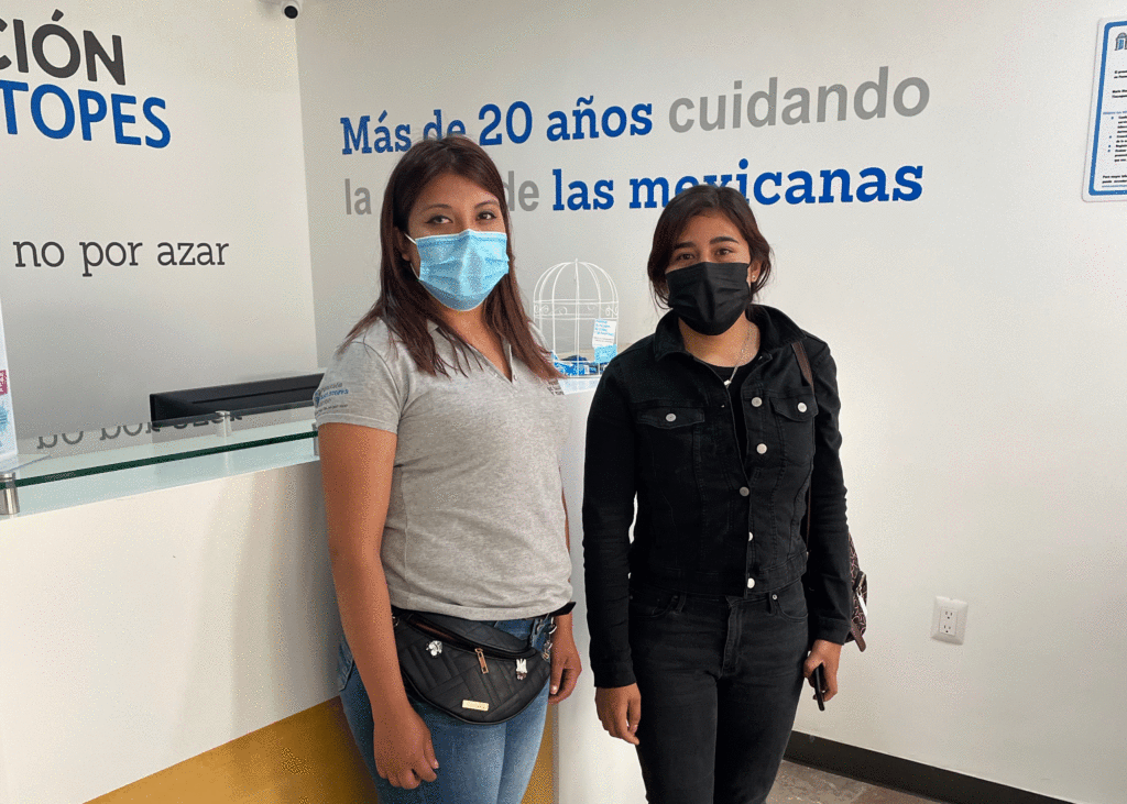 Two young Hispanic women wearing masks stand at an MSI clinic.