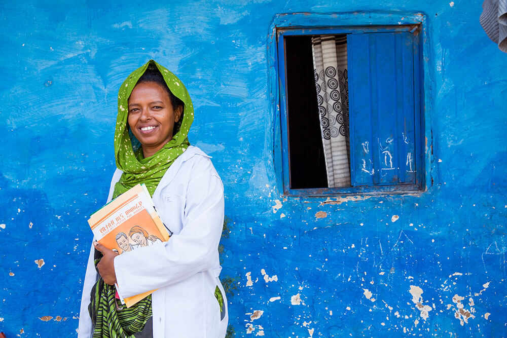 An Ethiopian medical provider in a green head scarf stands in front of a bright blue wall.