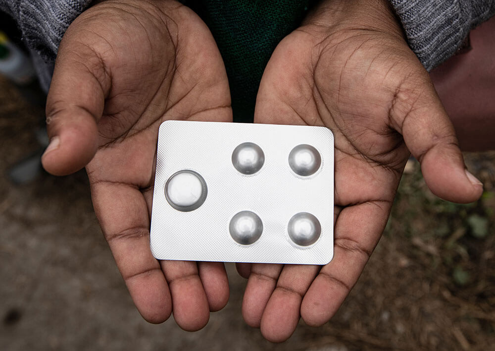 A pair of hands holds a blister pack with one large pill and four small ones.