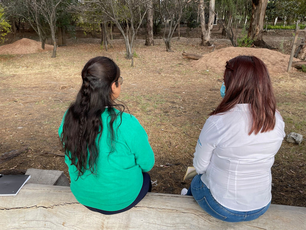Two Mexican women sit with their backs to the camera. They are sitting outdoors and having a conversation.