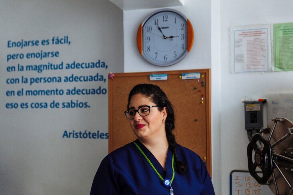 A woman doctor stands in a healthcare clinic. A Spanish-language quote about freedom to choose is on the wall behind her.