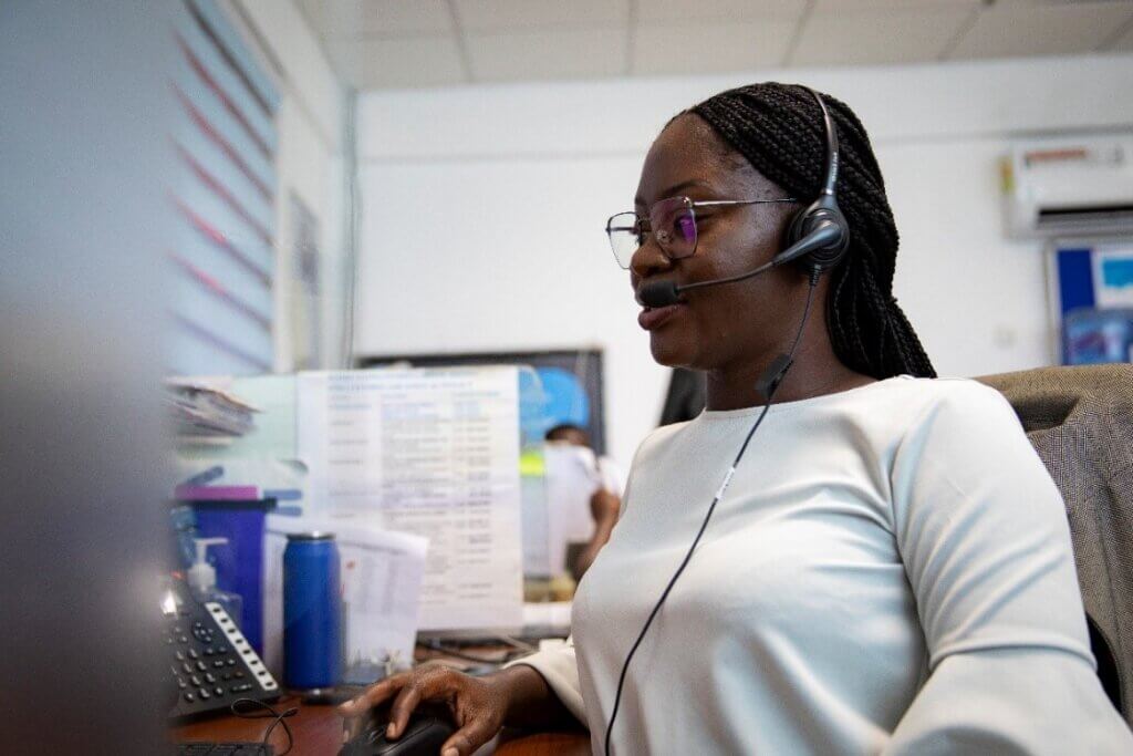 A woman wears a headset and works at a computer at a call center.